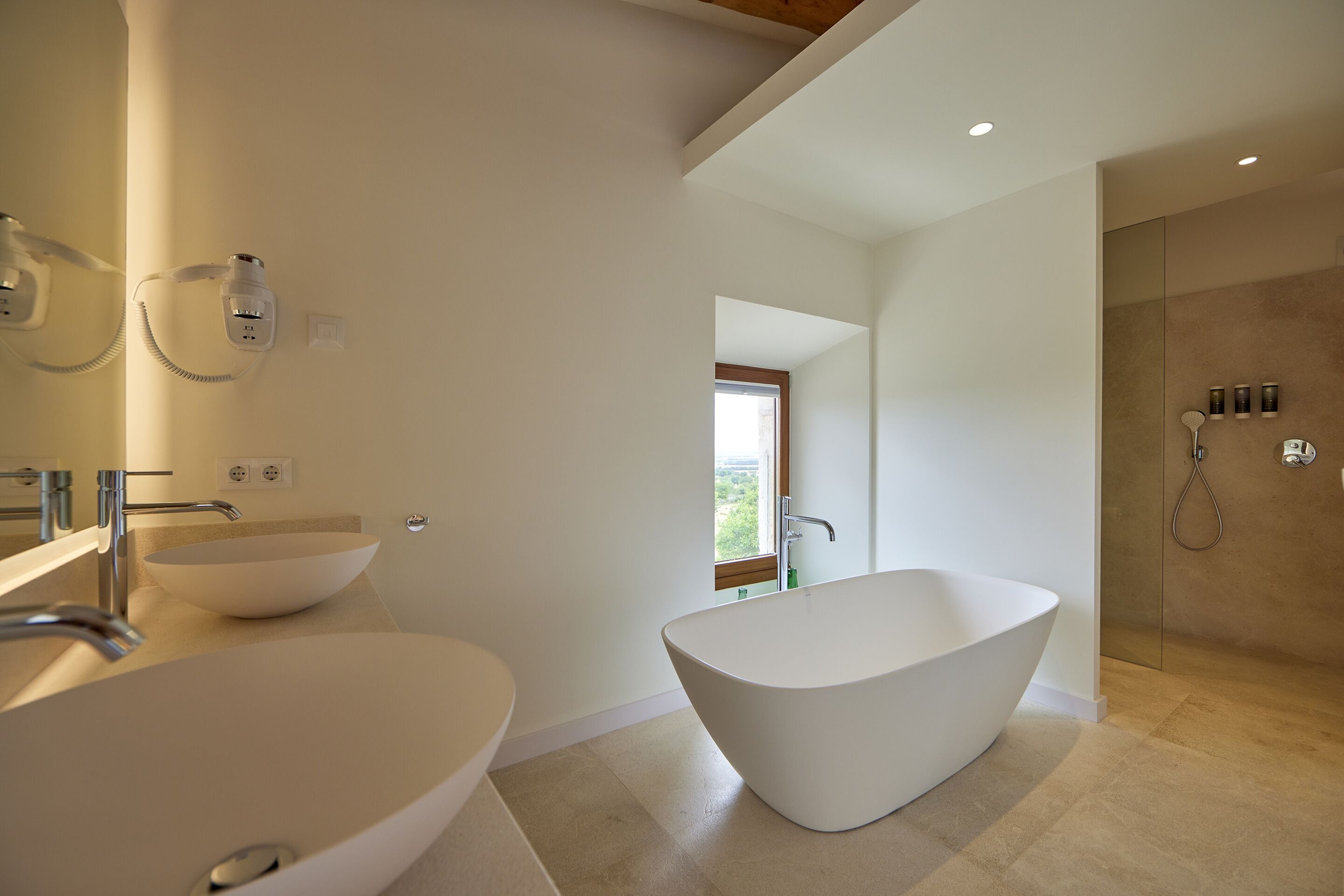 A modern bathroom with two large white sinks, a freestanding bathtub, and a walk-in shower.