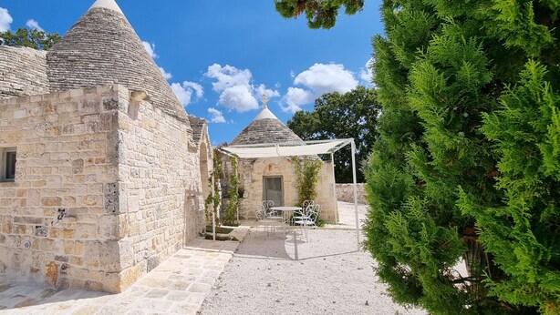 Un edificio de piedra con techo cónico, un patio de grava y una zona de estar exterior blanca.