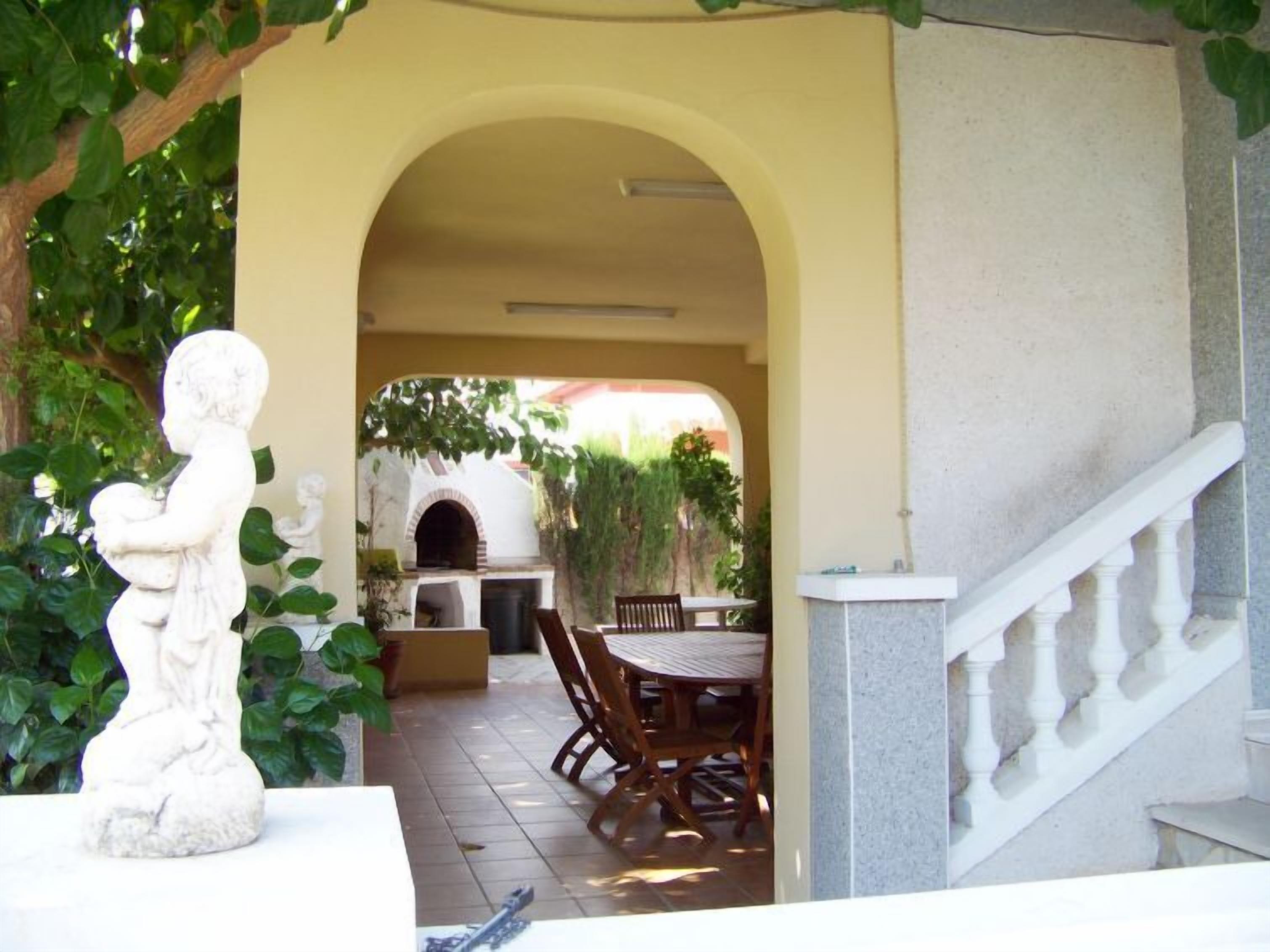 Eine Terrasse mit einer Steinstatue, einem Backofen aus Ziegeln und einem Esstisch mit Stühlen.