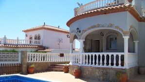 Vista a la piscina de un edificio con fachada blanca, tejas de terracota y un balcón con barandilla blanca.
