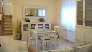 Una habitación pequeña y bien iluminada con una mesa de comedor y sillas, un mueble con puertas de vidrio, un espejo y una escalera que sube a otro nivel.