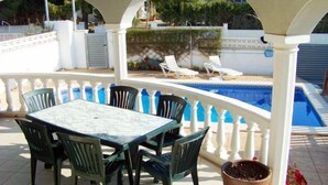 Un espacio exterior techado con piscina, una mesa con sillas y una planta en maceta.