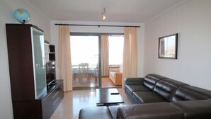 Un salon moderne avec un canapé en cuir marron foncé, un téléviseur à écran plat posé sur un meuble en bois et un balcon agrémenté de rideaux.