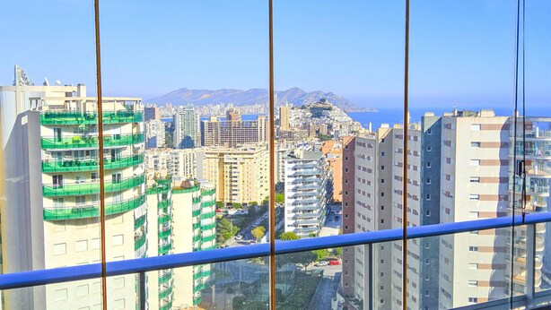 Un immeuble de grande hauteur doté de nombreux balcons, offrant une vue dégagée sur le paysage urbain, et dont on aperçoit l’espace piscine à travers la fenêtre.