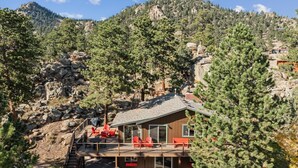 A cabin with a deck, red chairs, and a mountain backdrop.