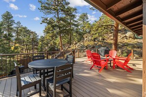 Eine Holzterrasse mit rundem Tisch und Stühlen, umgeben von Bäumen und einer felsigen Landschaft.
