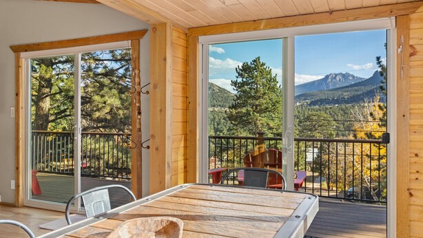 A wooden deck with a table and chairs, large sliding glass doors leading to a balcony with a mountain view.