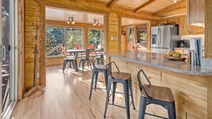 A spacious wooden cabin interior with a kitchen area, dining table, and bar stools.