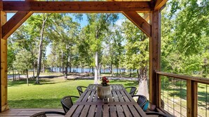 A wooden deck with a table and chairs, overlooking a lake and trees.