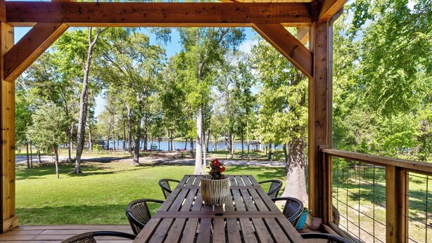 A wooden deck with a table and chairs, overlooking a lake and trees. - Stargazer Waterfront Luxe Retreat ✨Sand Beach 🎣Awesome Fishing🔥Campfires🛶Kayaks (Mineola)