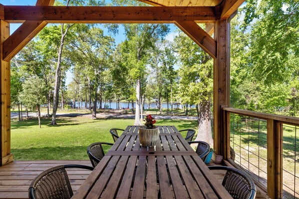 Una terraza de madera con una mesa y sillas, con vista a un lago y árboles.