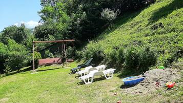 A grassy outdoor area with a swing set, a small shed, and several white plastic chairs.