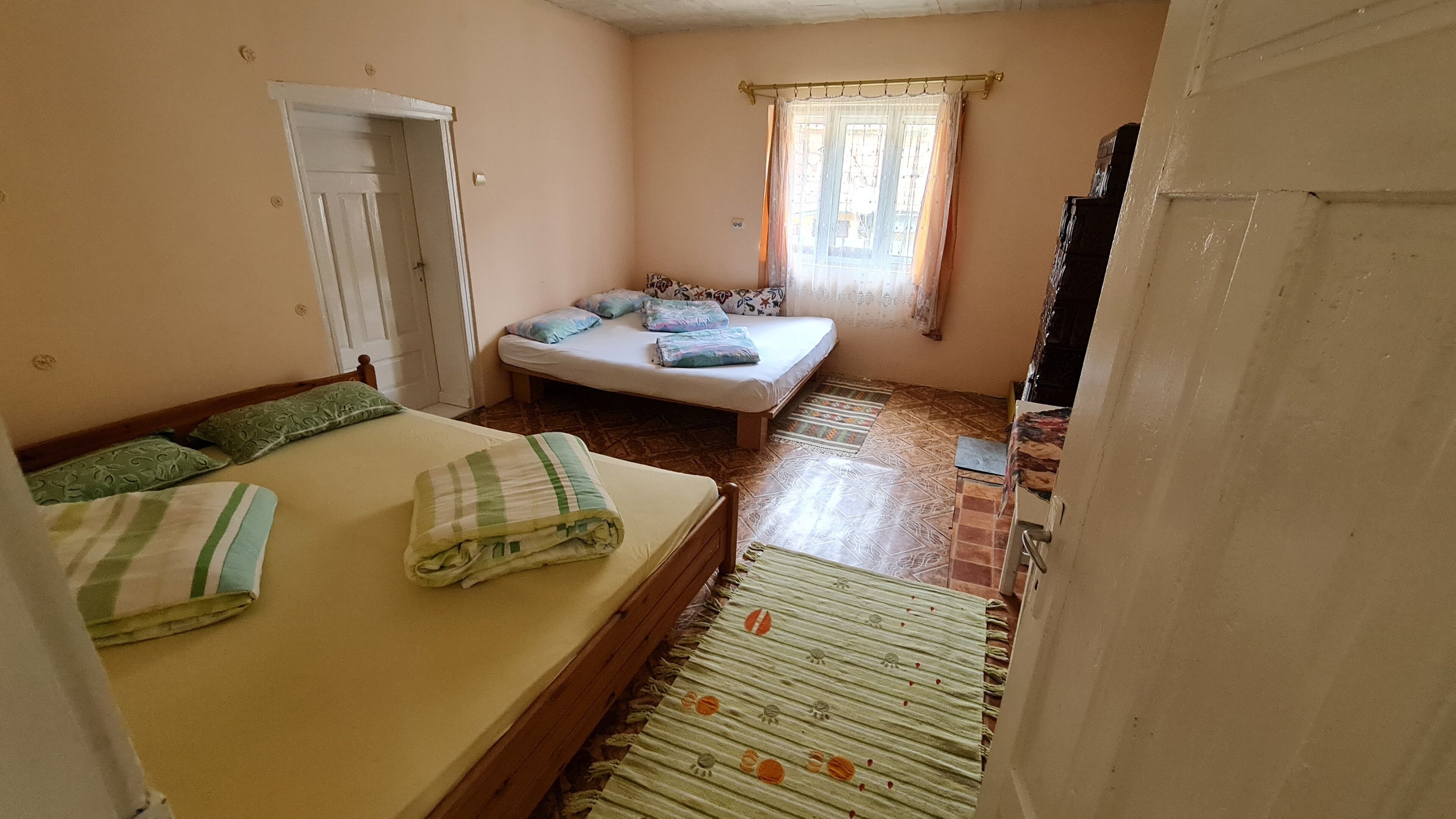 A small, cozy room with two beds, a window with curtains, and a tiled floor.
