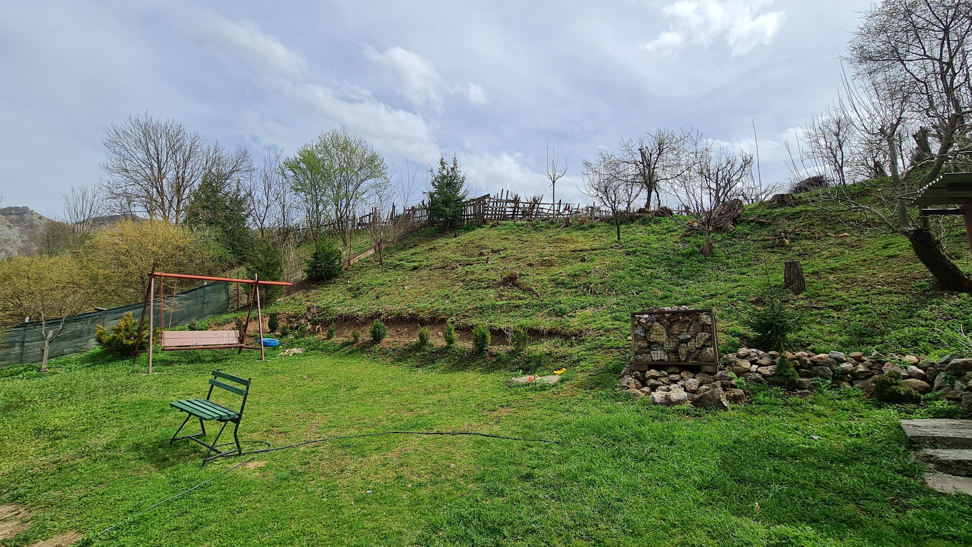 A grassy outdoor area with a swing set, a bench, and a stone structure.