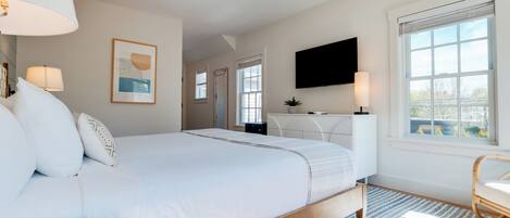 A modern bedroom with a large bed, bedside lamps, a desk, and a TV.