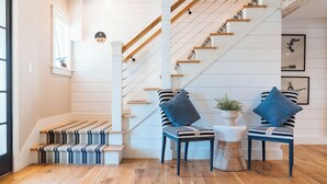 Eine Treppe mit Holzstufen und einem Streifenmuster-Teppich, zwei Stühle mit blauen Kissen und ein kleiner runder Tisch mit einer Pflanze.