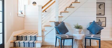 A staircase with wooden steps and a striped carpet, two chairs with blue cushions, and a small round table with a plant.