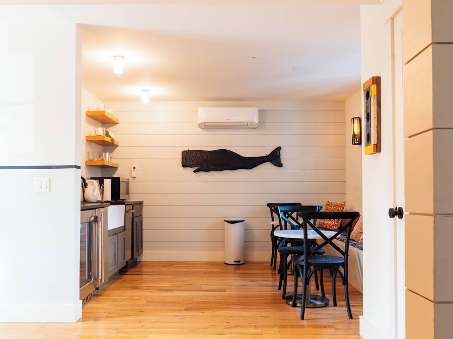 A compact kitchen with wooden flooring, white cabinets, a microwave, and a hanging fish sculpture.