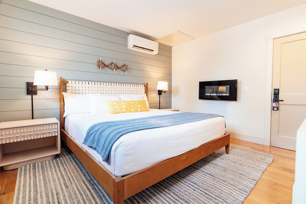 A modern bedroom with a wooden bed, two bedside tables with lamps, a mounted TV, and an air conditioning unit.