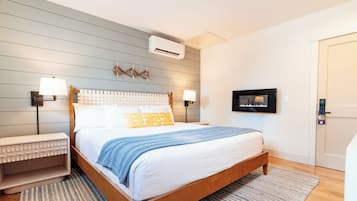 A modern bedroom with a wooden bed, two bedside tables with lamps, a mounted TV, and an air conditioning unit.