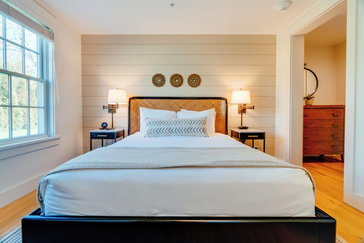 A neatly made bed with a headboard, two bedside tables with lamps, and a dresser to the right.