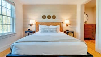 A neatly made bed with a headboard, two bedside tables with lamps, and a dresser to the right.