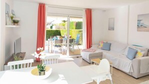 A bright living room with a sofa, a dining table, and a TV. There is a sliding glass door leading to an outdoor area with a table and chairs. - Bon Retorn by Interhome (L'Escala)