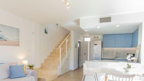 A modern living room with a staircase, a dining area with white chairs and a table, and a kitchen with blue cabinets. - Bon Retorn by Interhome (L'Escala)