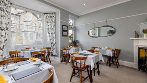 A dining area with multiple tables set for service, wooden chairs, a fireplace, and a large mirror on the wall. - 2 Cambridge Villas (Ambleside)