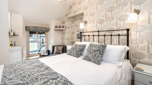 A bedroom with a bed, bedside tables, a nightstand, a window with a view, and a wall with a tree pattern. - 2 Cambridge Villas (Ambleside)