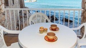 Ein runder Tisch mit zwei Tassen und zwei Gebäckstücken auf einem Balkon mit Blick aufs Meer.