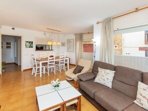 A living room with a brown sofa, a white coffee table, and a dining area with a wooden table and white chairs.