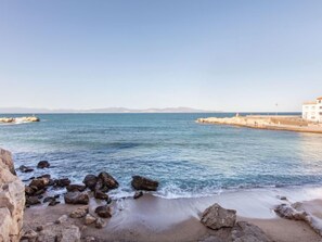 A coastal scene with a sandy beach, rocky shoreline, and a white building with a red roof.