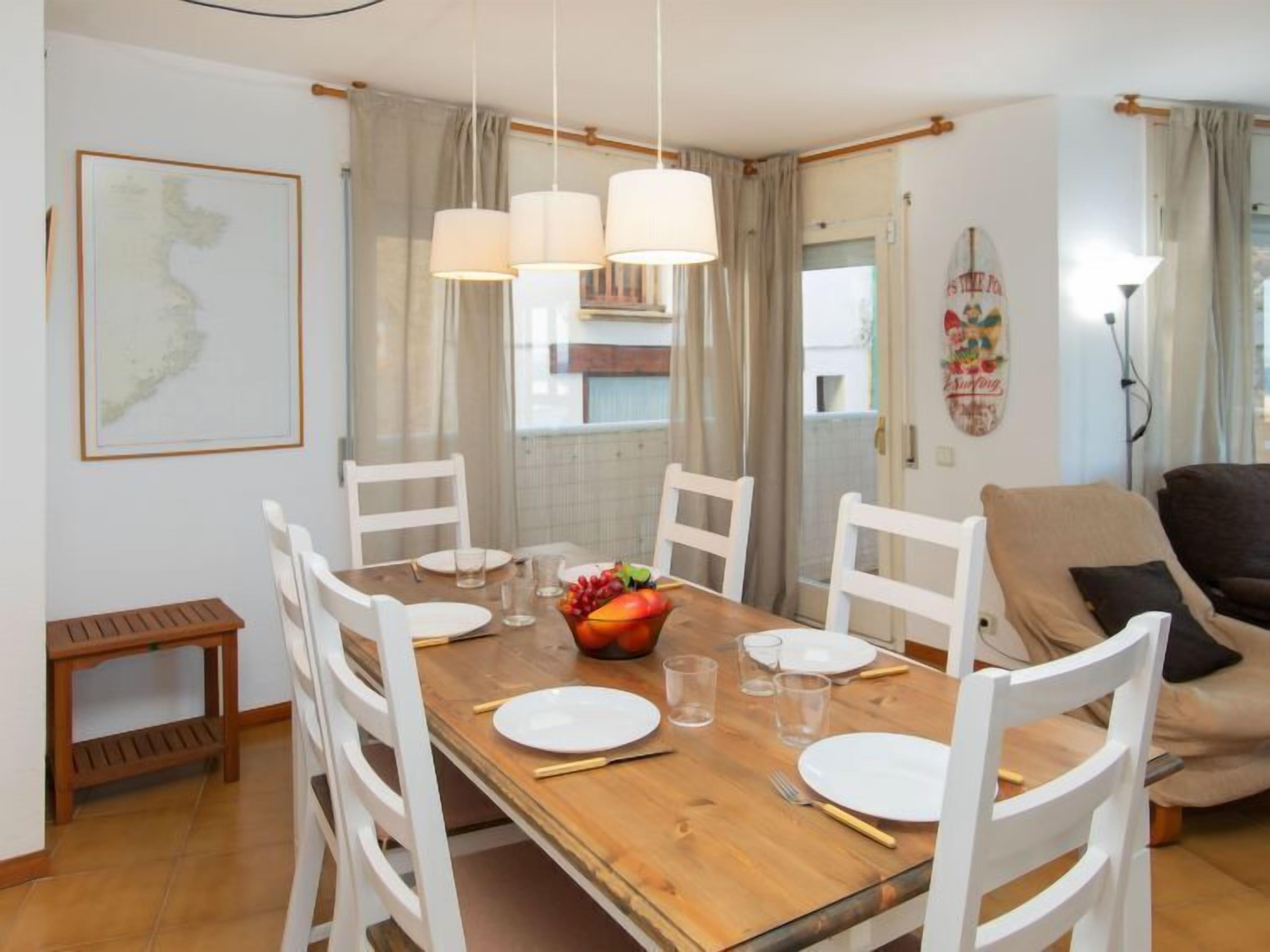 A dining area with a wooden table, white chairs, and hanging pendant lights.