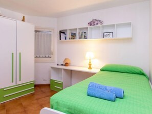 A bedroom with a bed, a desk, a wardrobe, and a shelf with books and decorative items.