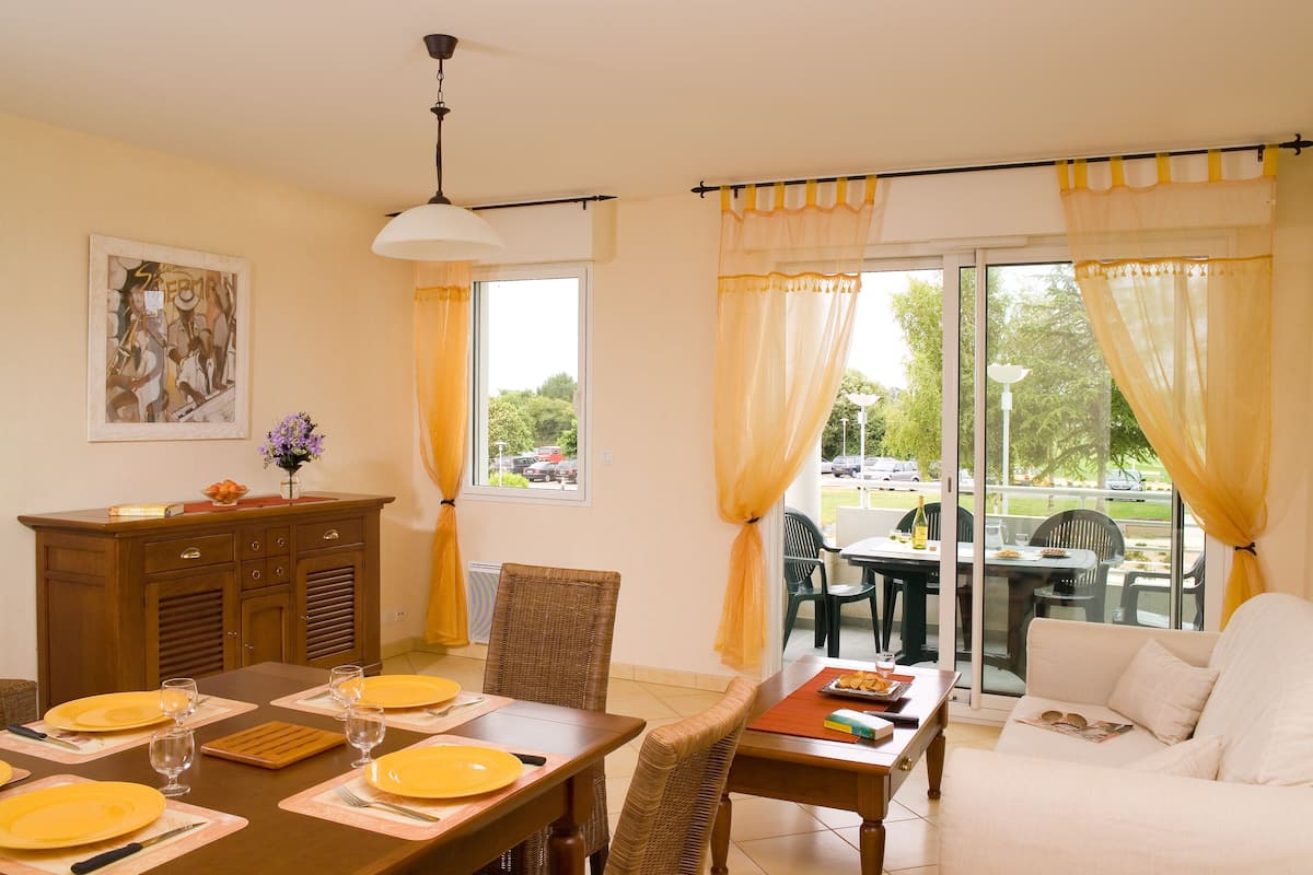Un coin repas avec une table dressée pour quatre personnes, un canapé et une fenêtre avec des rideaux.