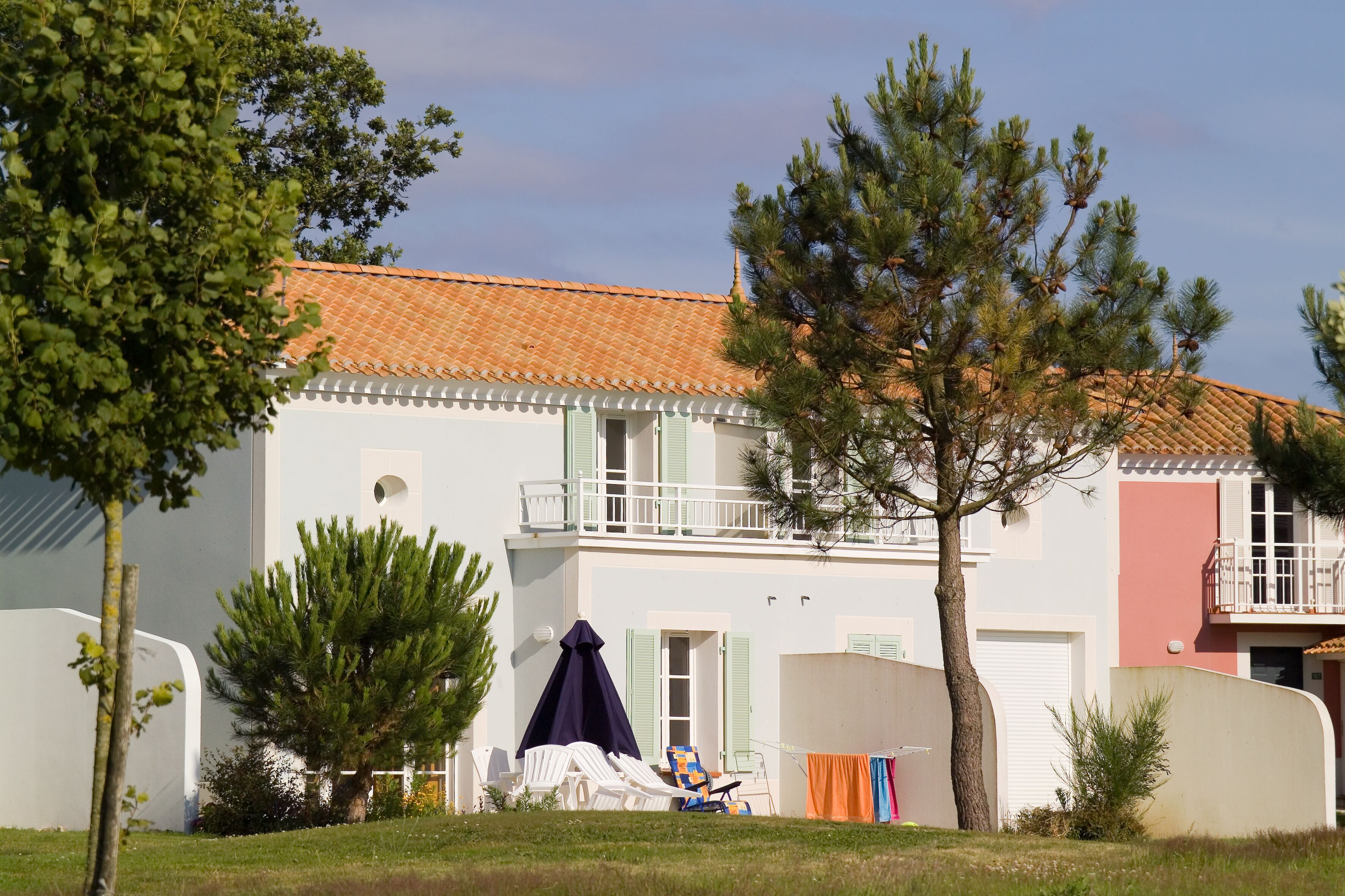 Une maison à deux étages, avec un toit en tuiles, un balcon et un espace extérieur aménagé avec des sièges.
