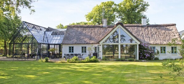 A thatched-roof house with a glass conservatory and a large lawn.