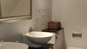 Et badeværelse med en hvid vask, et spejl, et hvidt toilet og en fletkurv på bordpladen.