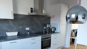 A modern kitchen with white cabinets, a black countertop, and a wooden dining table. - Fewo Provinzperle - newly designed - an ideal starting point for your tours (Freckenfeld)