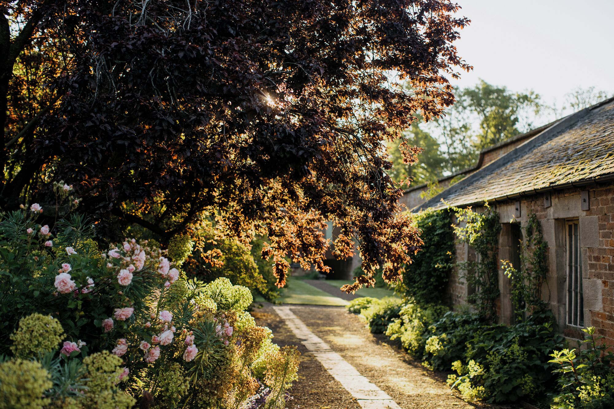 A garden pathway leading to a rustic building with a brick facade and a sloped roof.