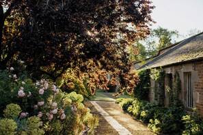 Un sentier de jardin mène à un bâtiment rustique doté d’une façade en briques et d’un toit en pente.
