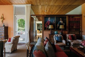 A well-lit living room with a wooden ceiling, a large painting, and a bookshelf filled with books.