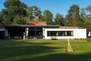A modern house with a large lawn, a tennis court, and a patio area with outdoor furniture.