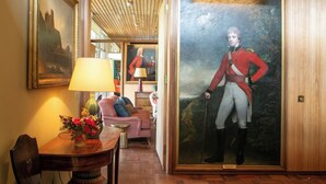 A room with a wooden floor, a dining table with a vase of flowers, a sofa, and a large framed portrait of a historical figure.