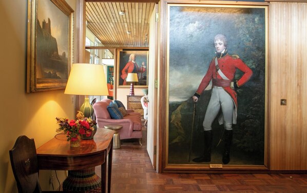 A room with a wooden floor, a dining table with a vase of flowers, a sofa, and a large framed portrait of a historical figure. - Luxury mid-Century  home in 5 acre garden close to superb golf courses & beaches (North Berwick)