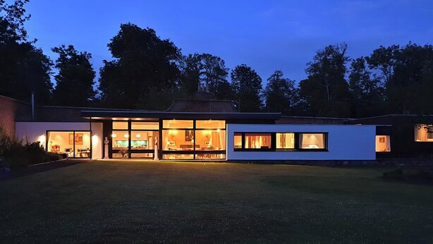 A modern house with large glass windows, a spacious lawn, and a brick exterior.
