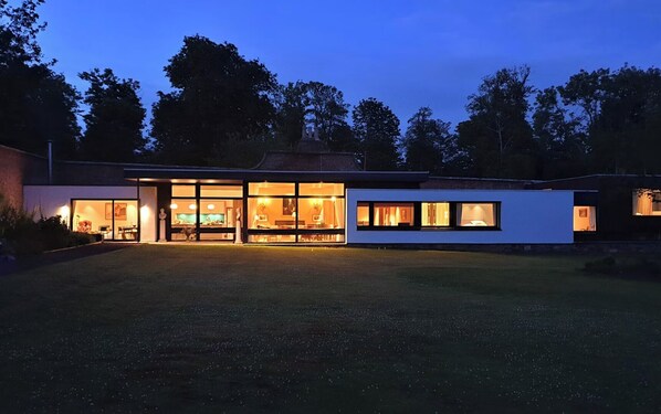 A modern house with large glass windows, a spacious lawn, and a brick exterior.