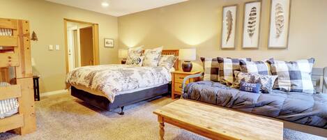 A bedroom with a bed, a sofa, a wooden table, and a wall with feather art.