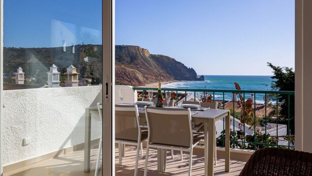A balcony with a table set for two, overlooking a coastal landscape with cliffs and the sea. - Waterside Village Townhouse (Luz)